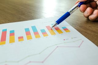 A person's hand using a pen to point to performance metrics on a graph.